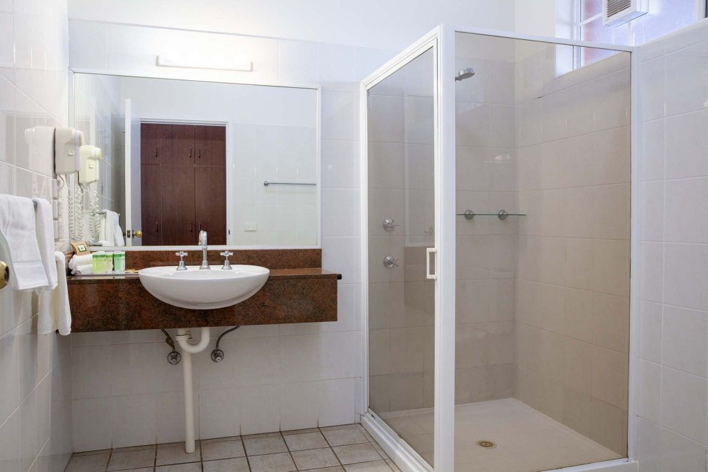 The Kidman Wayside Inn bathroom featuring a walk-in shower with a glass door and a wall-mounted sink on a granite countertop.