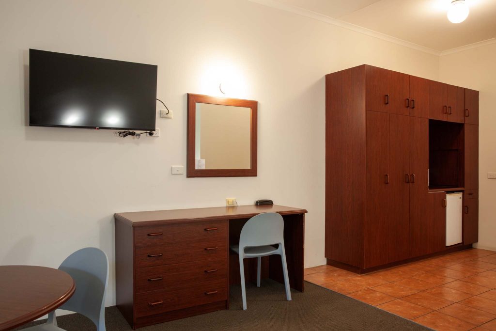 The Kidman Wayside Inn room featuring dark wood furniture, including a desk with drawers, a large wardrobe, and a small refrigerator.