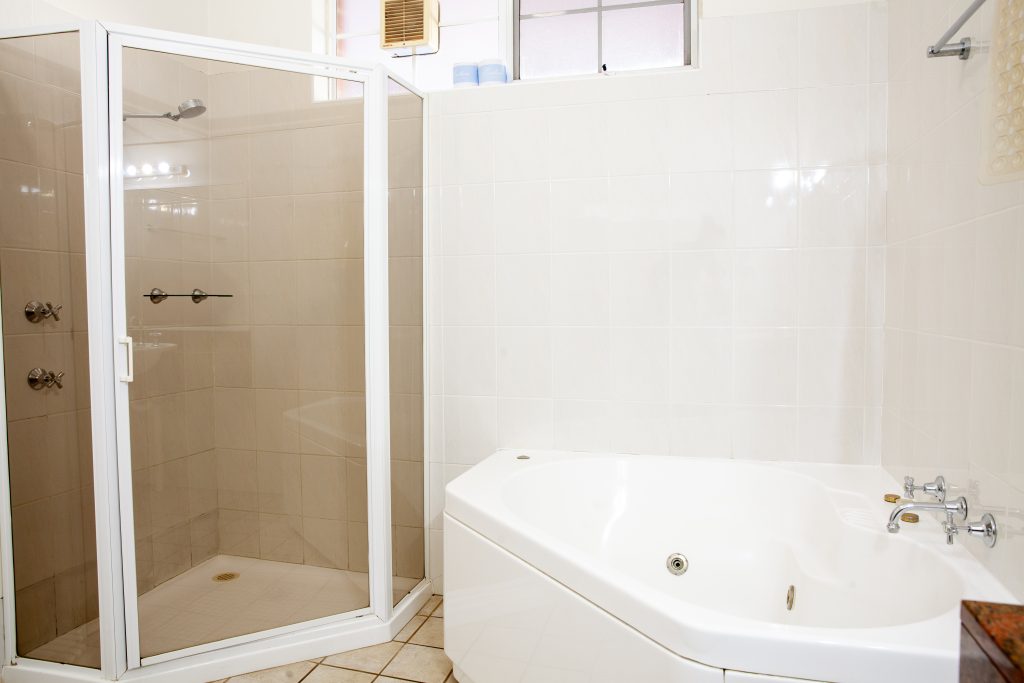 The Kidman Wayside Inn white-tiled bathroom featuring a glass-enclosed walk-in corner shower and a large white jetted soaking tub.