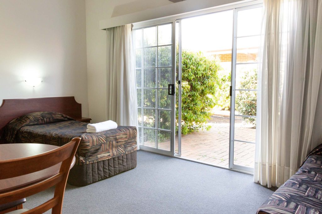 A brightly lit motel room featuring a single bed with a patterned brown bedspread