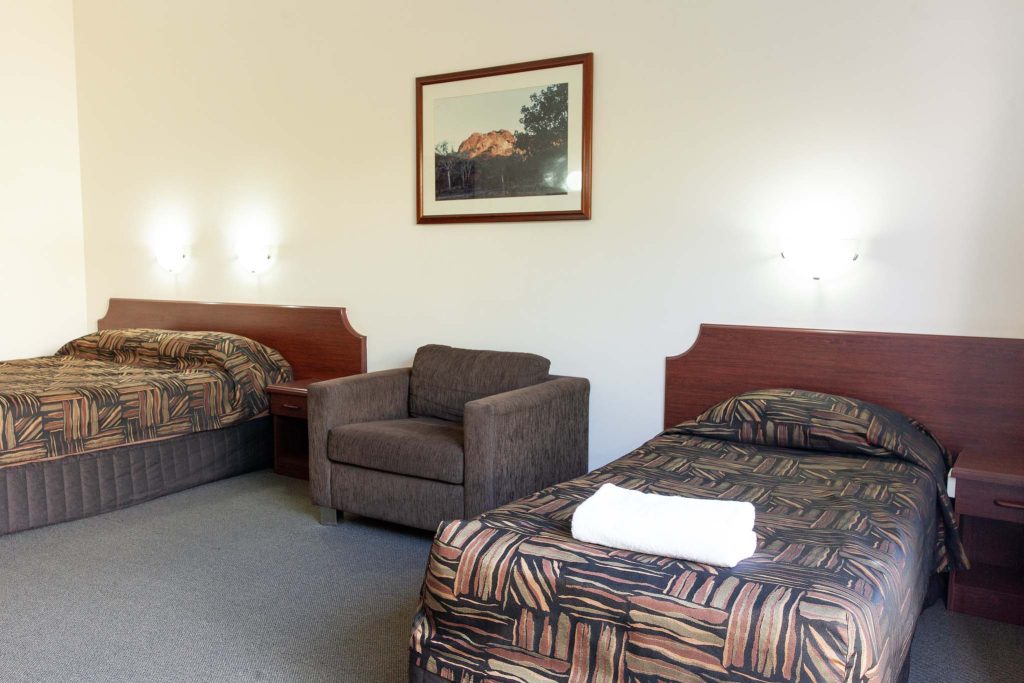 A hotel room featuring two beds with patterned brown bedspreads