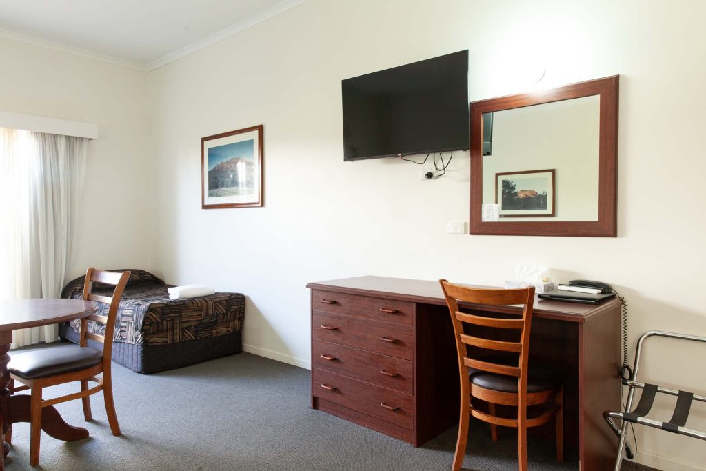 A simple hotel room featuring dark wood furniture, including a desk with a chair and a matching dresser.