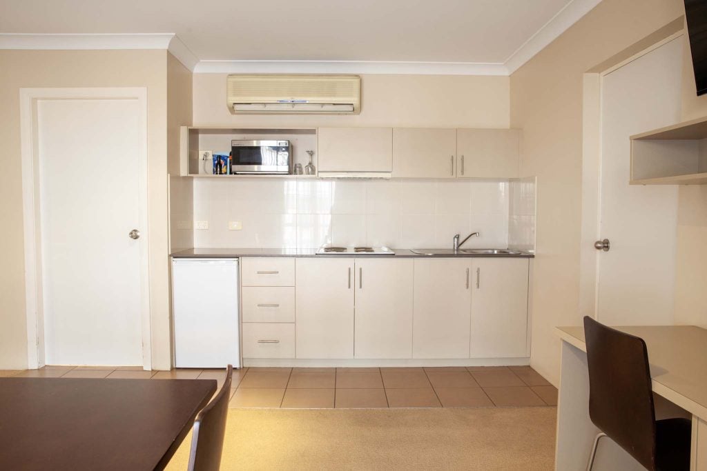 The Kidman Wayside Inn suite featuring a kitchenette with a stovetop and sink, a small dining table, and a workspace with a desk and microwave.