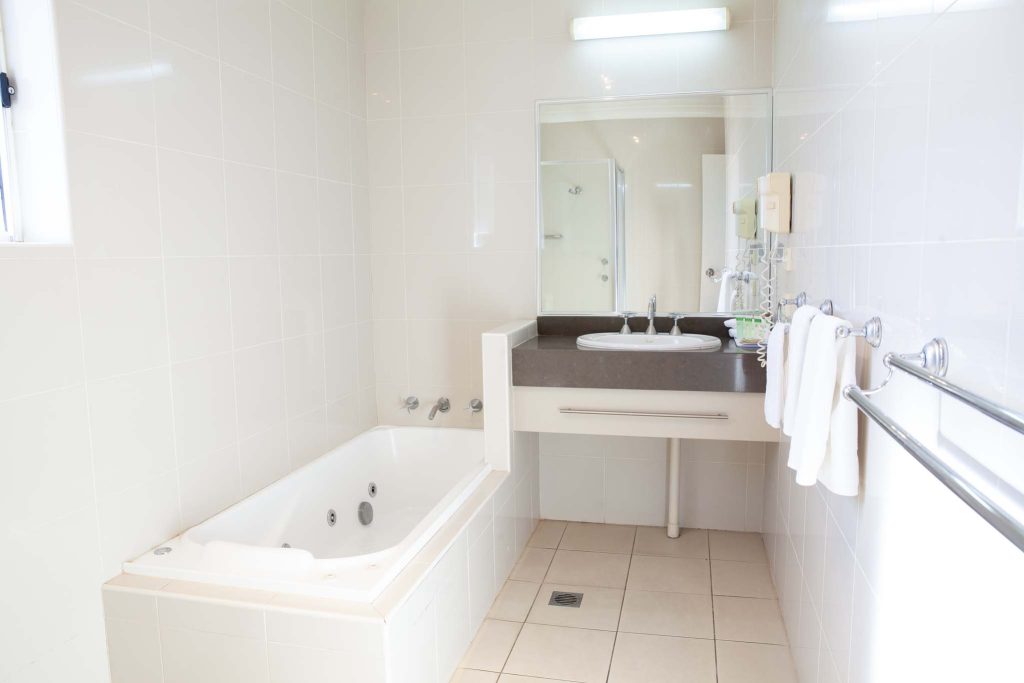 The Kidman Wayside Inn white-tiled bathroom including a large spa-style bathtub, a vanity with a dark countertop and large mirror