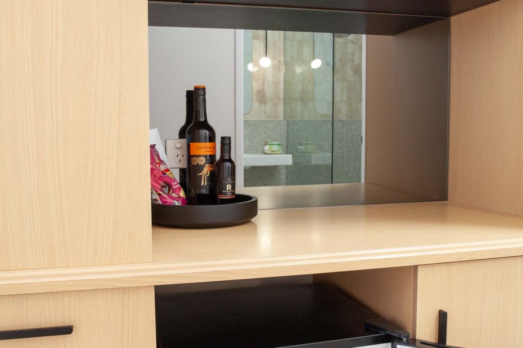 The Kidman Wayside Inn modern kitchen nook with light wood cabinetry featuring a small open refrigerator stocked with drinks, a counter with wine bottles.
