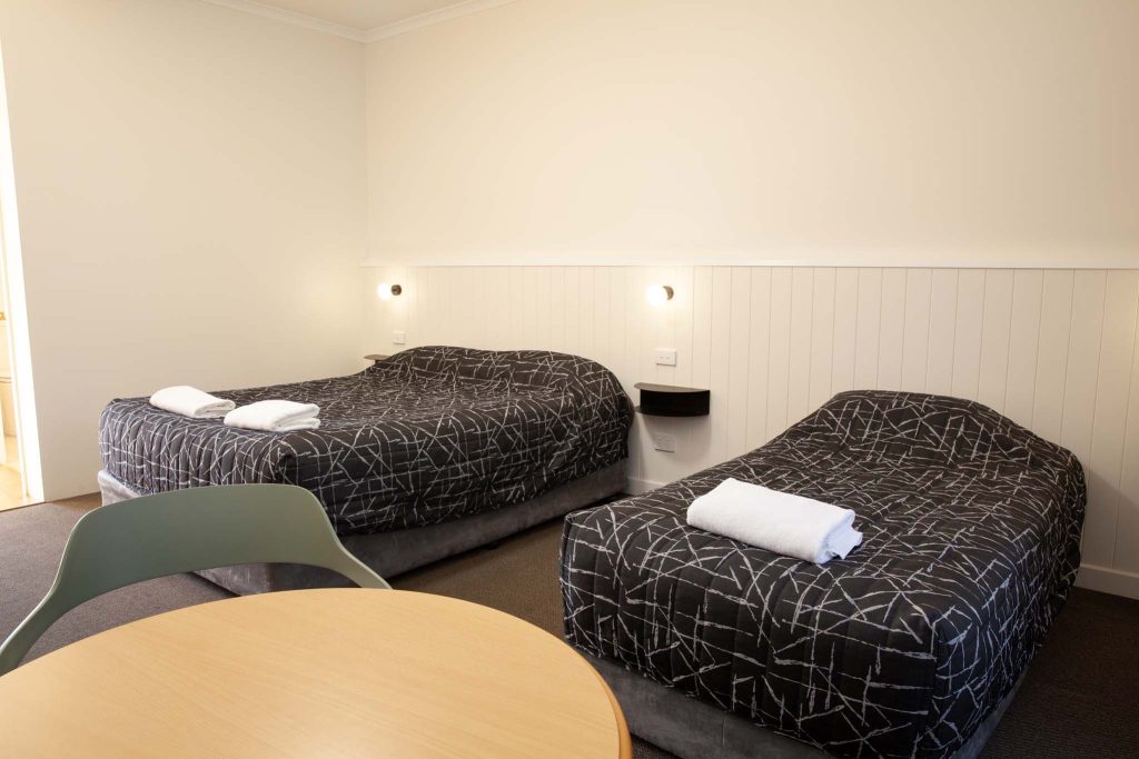 the kidman wayside inn room featuring one large bed and one single bed with dark patterned comforters and folded white towels.