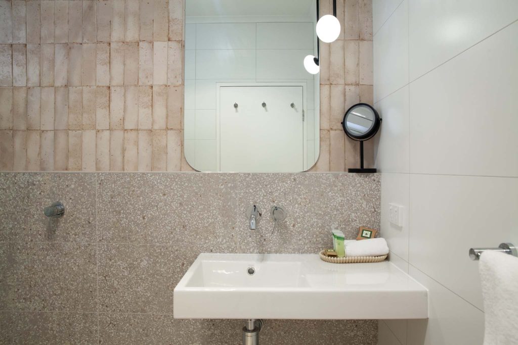 The Kidman Wayside Inn bathroom vanity featuring a white wall-mounted sink, a grey terrazzo-style tiled backsplash, and pink textured vertical tiles
