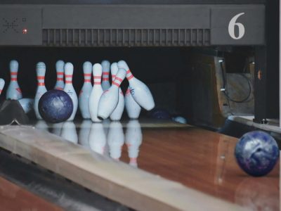 A close-up shot of a bowling lane where a blue bowling ball is hitting ten-pins