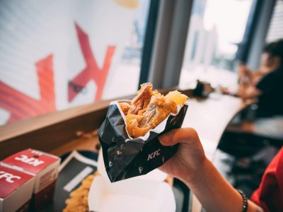 A person holding a partially eaten fried chicken wrap in a black KFC wrapper